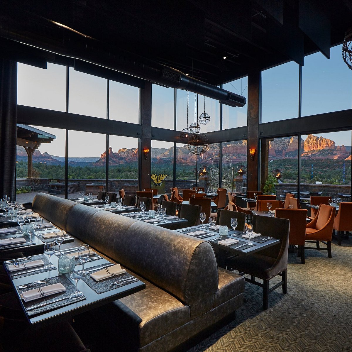 Elegant Sedona restaurant dining room with floor-to-ceiling windows overlooking red rock formations at dusk
